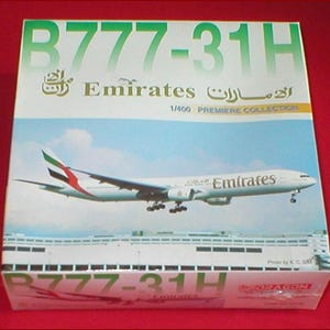 May include: A model airplane box featuring a Boeing 777-31H Emirates aircraft. The box is white with green and gold text, including "B777-31H" and "Emirates." The image on the box shows the plane in flight, with a blue sky background.
