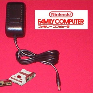May include: A black Nintendo Family Computer power adapter with a black cable, a console, and a controller on a red background. The Nintendo logo and "FAMILY COMPUTER" text are visible.
