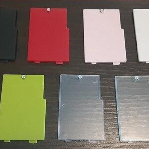 Puede incluir: Un conjunto de siete componentes rectangulares de plástico en varios colores: negro, rojo, rosa, blanco, verde y dos translúcidos. Cada pieza tiene un pequeño cierre metálico y un diseño con muescas. Los artículos están dispuestos sobre una superficie oscura.