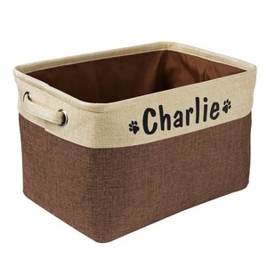 May include: A brown and beige fabric storage bin with a handle and the name "Charlie" printed on the front in black with paw prints.