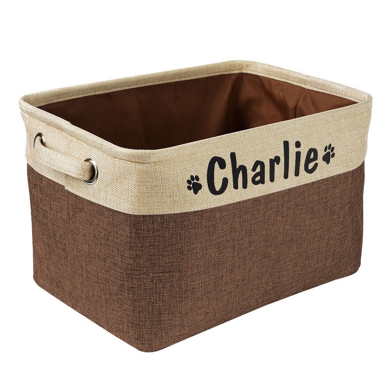 May include: A brown and beige fabric storage bin with a handle and the name "Charlie" printed on the front in black with paw prints.