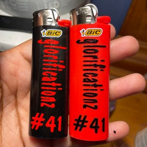 May include: Two red and black lighters with the word "glorification" and the number "#41" printed on them. Both lighters are BIC brand.