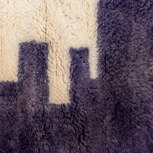 May include: Close-up of a textured rug with a geometric design. The rug has a deep purple background and a cream-coloured pattern. The design appears to be a series of connected shapes, creating a modern aesthetic.