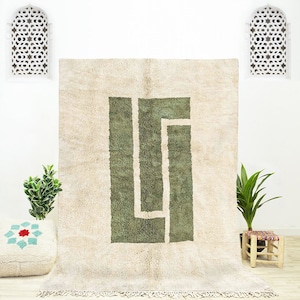 May include: A cream-coloured rug with a large green geometric design. The rug has a fringe border.