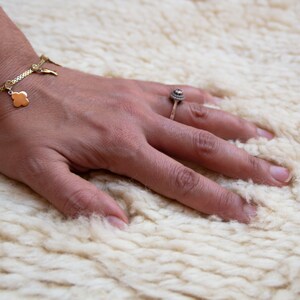 Puede incluir: Una mano con un brazalete dorado y un anillo de plata descansa sobre una superficie blanca y esponjosa.