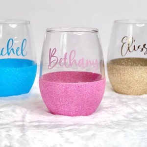 Op de afbeelding: Drie glazen wijnbekers van helder glas met glitterbodems. De bekers zijn gepersonaliseerd met de namen "Rachel", "Bethany" en "Elise".