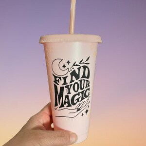 以下が含まれることがあります： 三日月と星が描かれた「Find Your Magic」という黒いデザインが施されたピンク色の再利用可能なカップ。ストロー付きです。