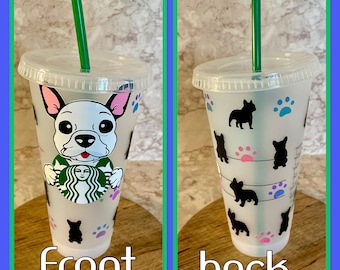 May include: A clear plastic reusable cup with a green straw. The front of the cup features a white French bulldog with a Starbucks logo. The back of the cup has a repeating pattern of black French bulldogs, paw prints, and stripes.