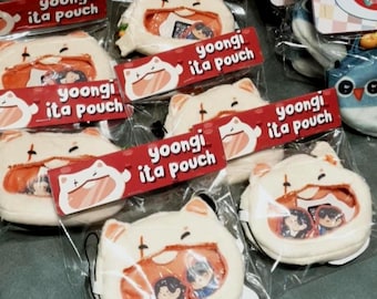 Op de afbeelding: Verschillende witte katvormige pouches met doorzichtige vensters, elk met kleine afbeeldingen. De pouches zijn verpakt in doorzichtige plastic zakken en hebben rode labels met de tekst "yoongi ita pouch".