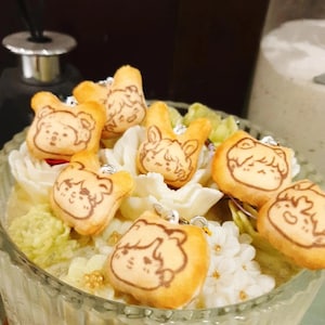 May include: A glass bowl filled with white and green floral arrangements.  The bowl is decorated with small, brown, cartoon-like animal charms.