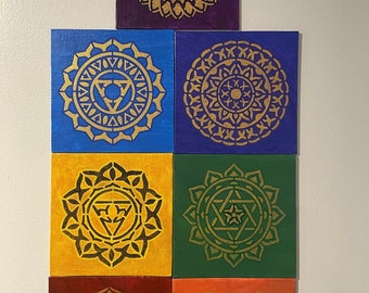 May include: Six square canvases with gold mandala designs on different colored backgrounds. The colors are purple, blue, yellow, green, red, and orange. Each mandala has a different symbol in the center.