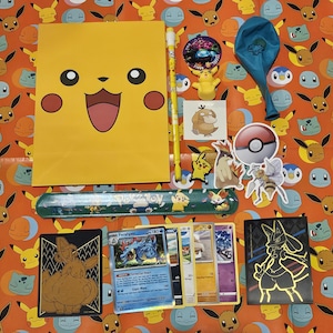 May include: A collection of Pokemon-themed items including a yellow folder with a Pikachu face, a blue ruler, a set of trading cards, a blue balloon, and stickers.