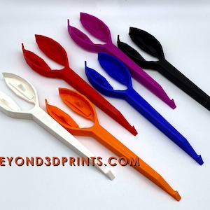 May include: Six different colored plastic tools with a unique design. The tools are white, orange, red, blue, purple, and black. The tools are all the same shape and have a curved handle and a pointed tip. The tools are arranged in a row from left to right, with the white tool at the left and the black tool at the right. The tools are all on a white surface. The text "BEYOND3DPRINTS.COM" is visible in the lower left corner of the image.