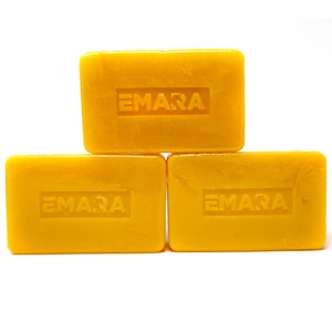 Puede incluir: Tres barras de jabón amarillas con la palabra "EMARA" en relieve en cada barra.