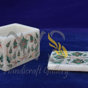 Può includere: Una scatola in marmo bianco con un motivo floreale verde e rosso. La scatola ha un coperchio incernierato ed è decorata con dettagli intricati.