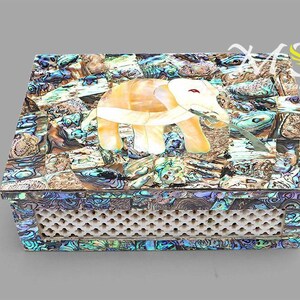 Puede incluir: Una caja decorativa hecha de nácar con un diseño de elefante incrustado. La caja tiene una base de celosía blanca.