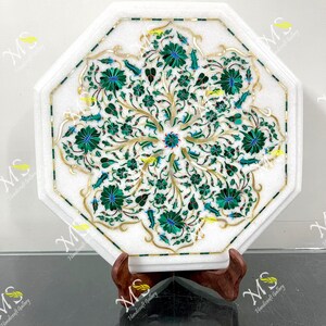 Op de afbeelding: Witte marmeren tafel met een achthoekige vorm, met een gedetailleerd bloemeninlegontwerp in groen, goud en blauw. De tafel wordt ondersteund door een houten standaard, die een mix van natuurlijke materialen en ingewikkeld vakmanschap laat zien.