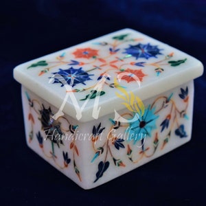Può includere: Una scatola di marmo bianco con un design floreale intarsiato con pietre colorate. La scatola è chiusa e ha un coperchio con cerniera.
