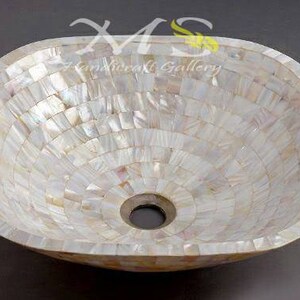 May include: A white ceramic sink with a decorative mother-of-pearl mosaic design. The sink has a round drain hole in the center.