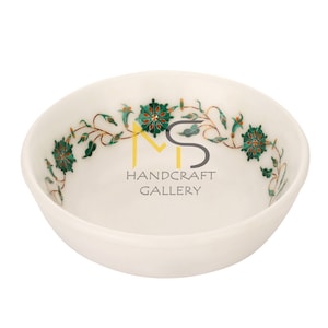 May include: White marble bowl with a green and gold floral design. The bowl is decorated with intricate details and is perfect for serving snacks or desserts.