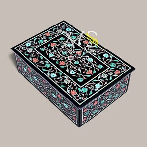 Può includere: Scatola in legno nero con un intricato design floreale intarsiato con pietre colorate. La scatola è chiusa e il coperchio è decorato con un motivo floreale.