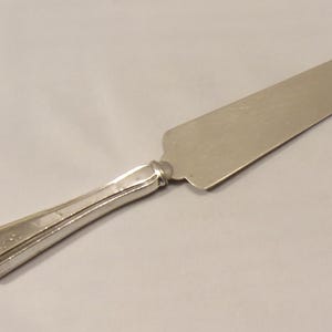 May include: Silver cake server with a long, thin blade and a detailed, ornate handle.