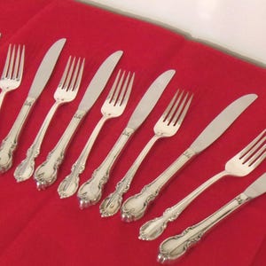 May include: A collection of silver-colored forks and knives arranged on a red surface. The silverware has ornate handles and a classic design, suitable for formal dining. The image showcases a set of ten pieces.