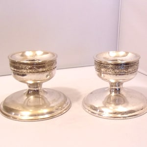 May include: Two silver candle holders with a round base and a detailed floral design around the top. The candle holders have a classic, elegant design, perfect for adding a touch of sophistication to any space.