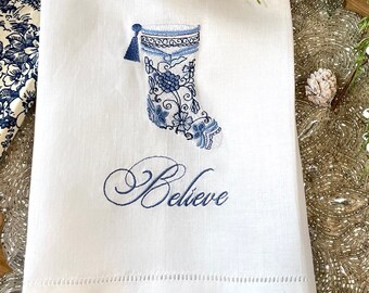 May include: White linen tea towel with blue embroidered stocking and the word "Believe".