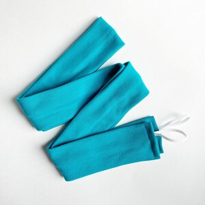 以下が含まれることがあります： 白いゴム紐が付いたターコイズブルーの布製のヘッドバンド。ヘッドバンドは折り畳んで結ばれています。