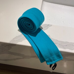 以下が含まれることがあります： 黒いストラップが付いた、ターコイズブルーの布のチューブが巻かれている