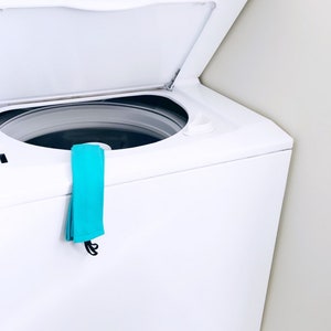 以下が含まれることがあります： 白い洗濯機に青い布が側面にかけられています。洗濯機にはGEのロゴと「Washer Dryer」の文字が前面に表示されています。画像の下部には「Easy to wear. Easy to wash.」という文字が青色で書かれています。