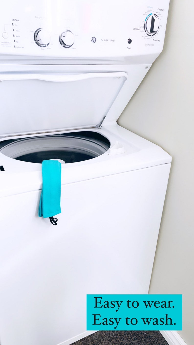 以下が含まれることがあります： 白い洗濯機に青い布が側面にかけられています。洗濯機にはGEのロゴと「Washer Dryer」の文字が前面に表示されています。画像の下部には「Easy to wear. Easy to wash.」という文字が青色で書かれています。