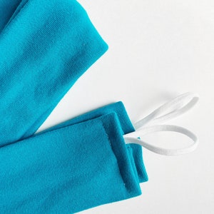 以下が含まれることがあります： 白いゴムひもが付いたターコイズブルーの布製の腕カバー2つ。腕カバーは折り畳まれて、ひもは一緒に結ばれています。