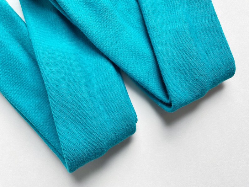 以下が含まれることがあります： ターコイズブルーの布地が2枚、折り畳まれています。布地は柔らかく、滑らかな質感です。