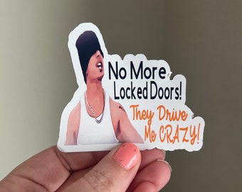 May include: A white sticker featuring a cartoon illustration of a person wearing a black beanie and a white tank top. The sticker has the text "No More Locked Doors! They Drive Me CRAZY!" in black and orange.