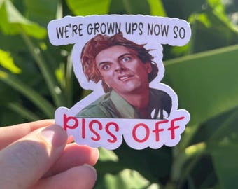 May include: A white sticker with the text "WE'RE GROWN UPS NOW SO PISS OFF" in black and red. The sticker features a photo of a man with a surprised expression.