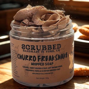 May include: A clear glass jar filled with brown whipped soap, topped with decorative swirls and glitter. The label reads "Churro Freakshake Whipped Soap" with caramel, cinnamon, and vanilla scents. Net weight is 100g.