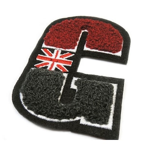 May include: A black, embroidered letter "G" patch with a red, fuzzy top section and a gray, fuzzy bottom section. The patch features a Union Jack flag design in the center, with white stitching around the edges.