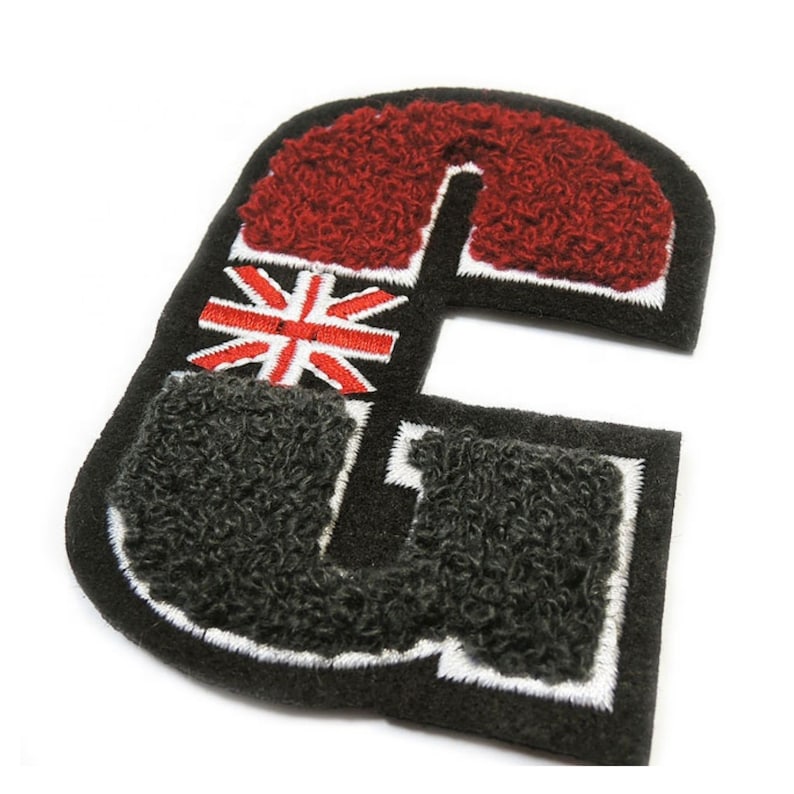 May include: A black, embroidered letter "G" patch with a red, fuzzy top section and a gray, fuzzy bottom section. The patch features a Union Jack flag design in the center, with white stitching around the edges.
