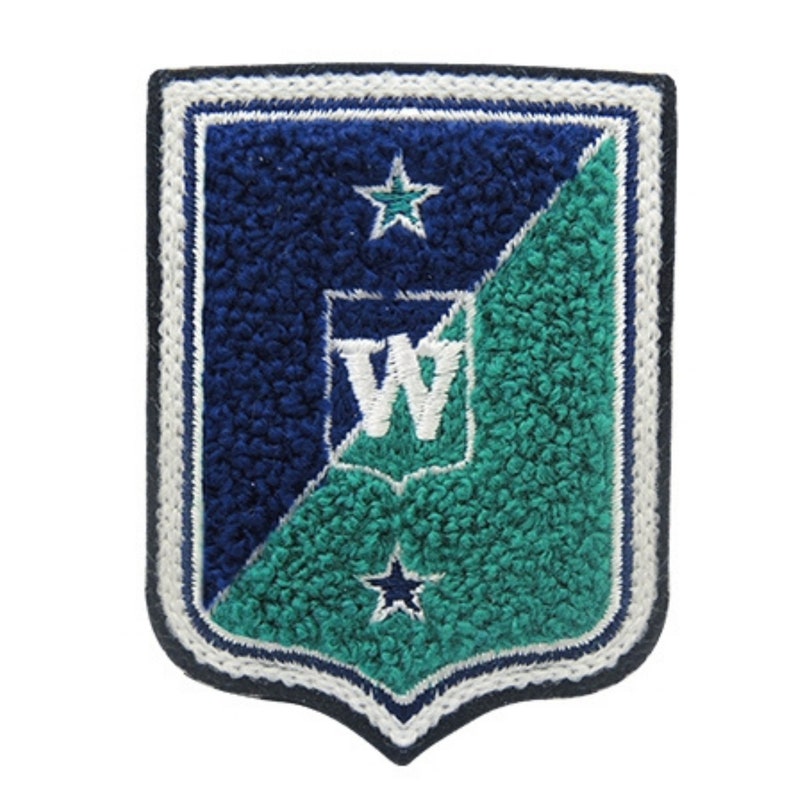 May include: A shield-shaped patch with a navy blue and teal design. The patch features a white embroidered border and a white letter "W" in the center. Two white stars are placed on the navy blue and teal sections.