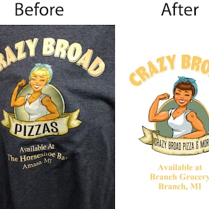 May include: A dark gray t-shirt featuring a cartoon image with the words "CRAZY BROAD PIZZAS" in gold lettering. The image includes a smiling woman flexing her arm. Below the image is the text "Available At The Horseshoe Bar Amasa, MI."