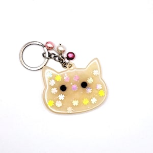 May include: A white resin cat keychain with a silver key ring and colorful flower accents. The cat has black eyes and a white background with colorful flowers.