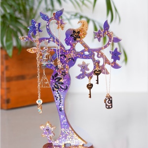 May include: Purple glitter tree-shaped jewellery stand with a woman silhouette, holding necklaces and key-shaped charms.