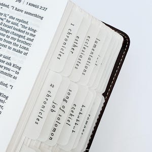 May include: Close-up of a Bible with white tabs labeled with book names. The tabs are inserted between the pages. The book is open to the text of 1 Kings 2:27.