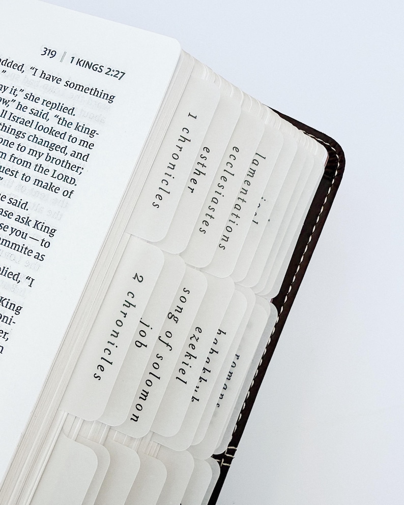 May include: Close-up of a Bible with white tabs labeled with book names. The tabs are inserted between the pages. The book is open to the text of 1 Kings 2:27.