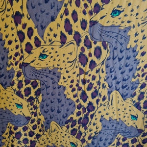 May include: A fabric with a repeating pattern of brown and yellow leopard print. The leopard spots are outlined in black and have a blue-green color in the center.