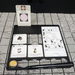 May include: A black and white character card game with a black plastic game board. The game board has a character sheet with the words "Survival", "Dodge", "Encourage", "Brain", "Head", "Arms", "Body", "Waist", "Legs", and "Notes".