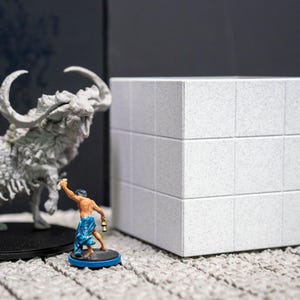 May include: A detailed image of miniature fantasy figures and a textured white cube. The figures include a large, horned beast and two small humanoids, each with unique paint details. The cube is composed of three stacked sections.