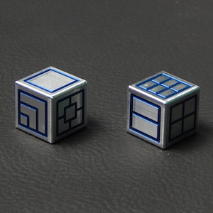 May include: Two silver metal dice with blue lines and geometric patterns. The dice are on a dark grey surface.